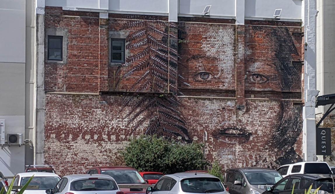 A subtle mural of the face of a girl fading into a brick wall, with a large fern next to her face