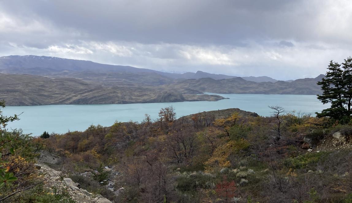 Blue lake, rocky path, green vegetation, rolling hill, and gray clouds