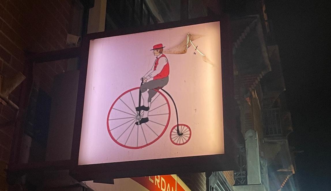 A sign of a man on an old fashioned bicycle with one large wheel 