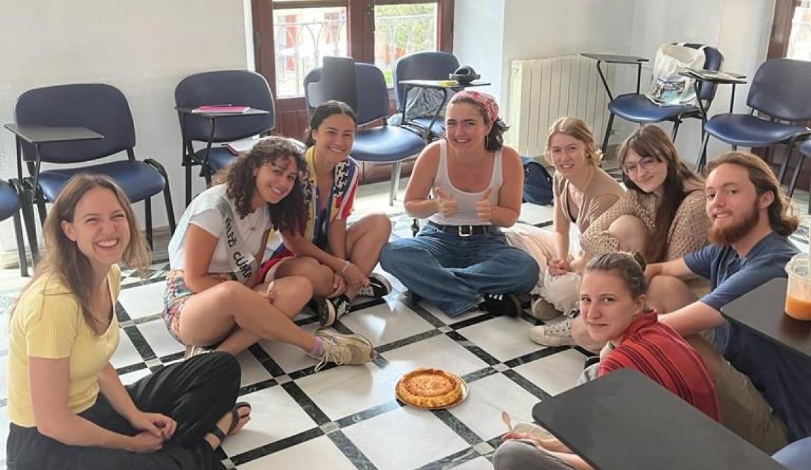 Spanish class sitting in a circle on the floor around a cheesecake.