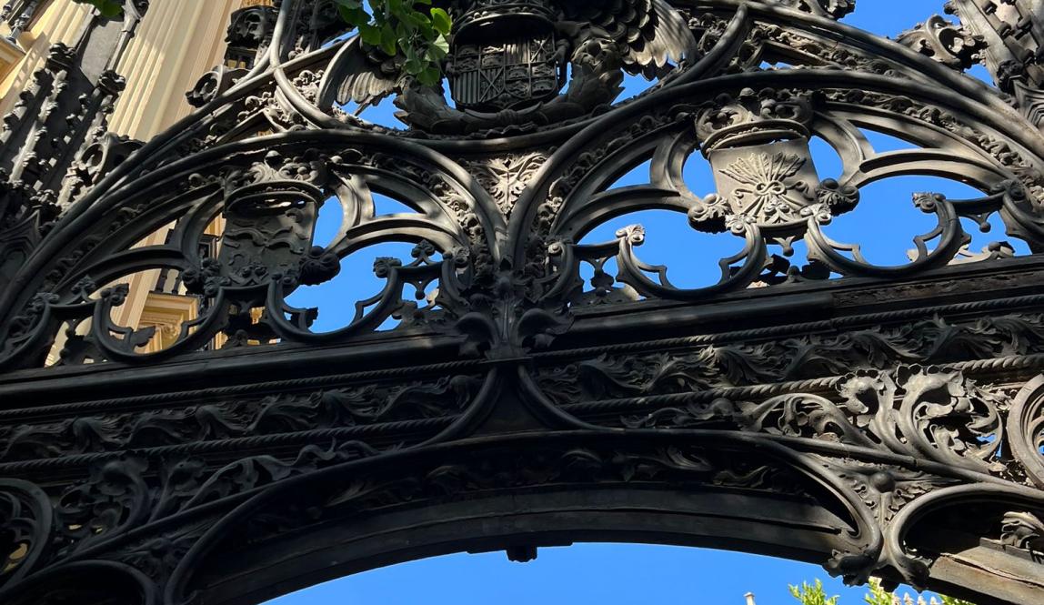 A bronze gothic style gate at the entrance to the Granada Cathedral courtyard, with trees in the background. 