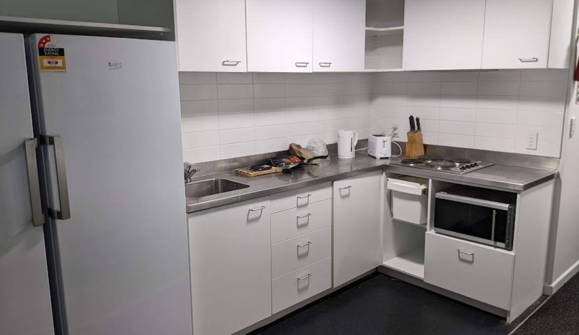 A kitchen with a large white fridge and freezer, white cupboards, and a steel countertop with a stovetop and microwave and sink.