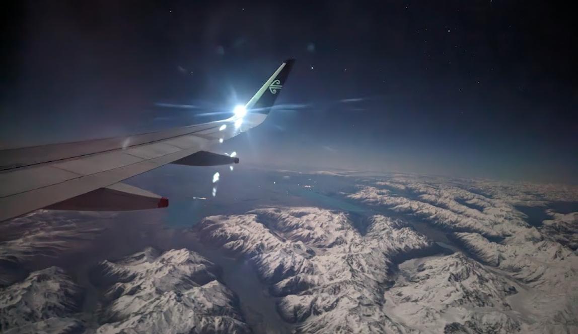 View from a plane at night of the Southern Alps of NZ, illuminated by the snow covering them