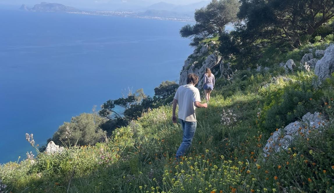 Two students hiking on a grassy mountain near the Mediterranean coast in Italy.