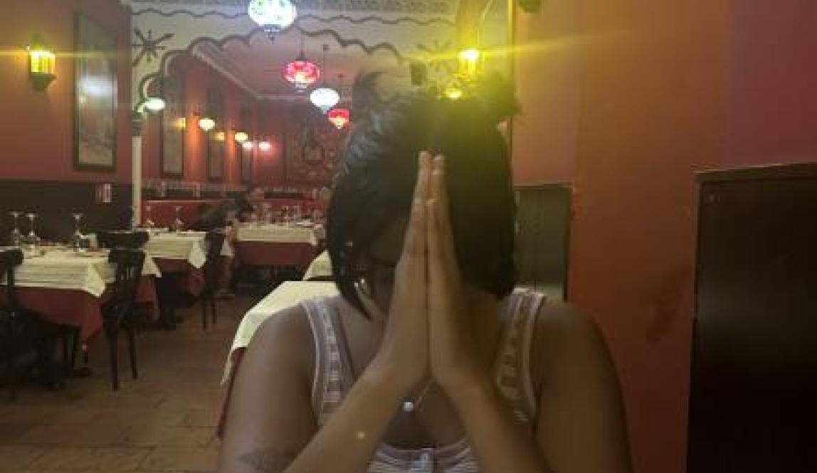 An image of me at a table in the Indian restaurant with my hands folded in prayer waiting for our food to arrive.