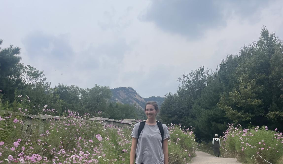 Image of student posing in front of flowers and fortress wall on hiking trail 
