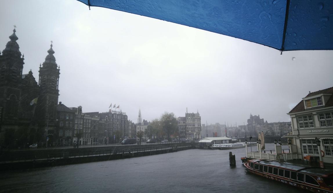 Amsterdam on a rainy morning, with the edges of a blue umbrella visible from the top-right corner and top edge.