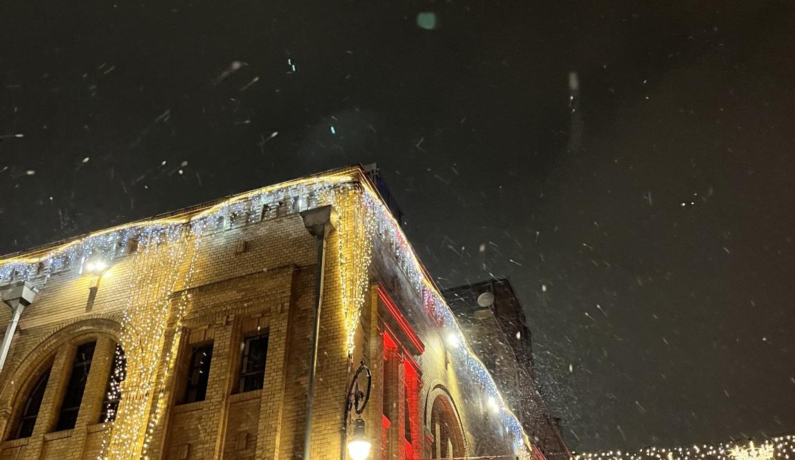 Christmas lights of yellow and white strung up around a square brick building in the snow