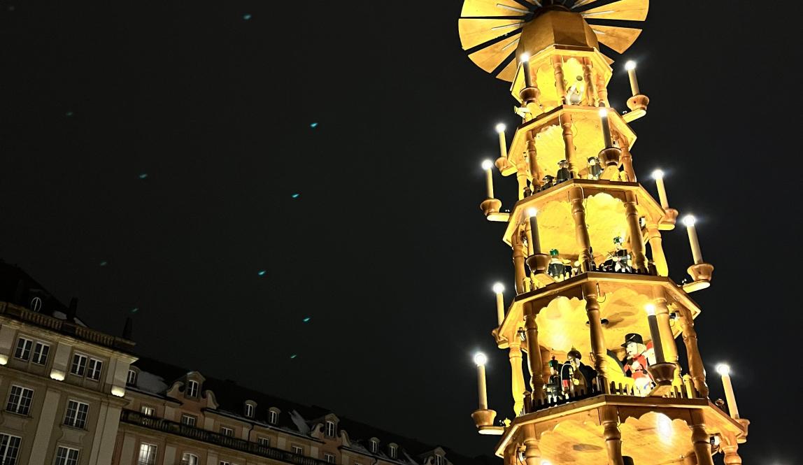Tower of lights that resembles a church is in a town square with Christmas Lights hanging from it