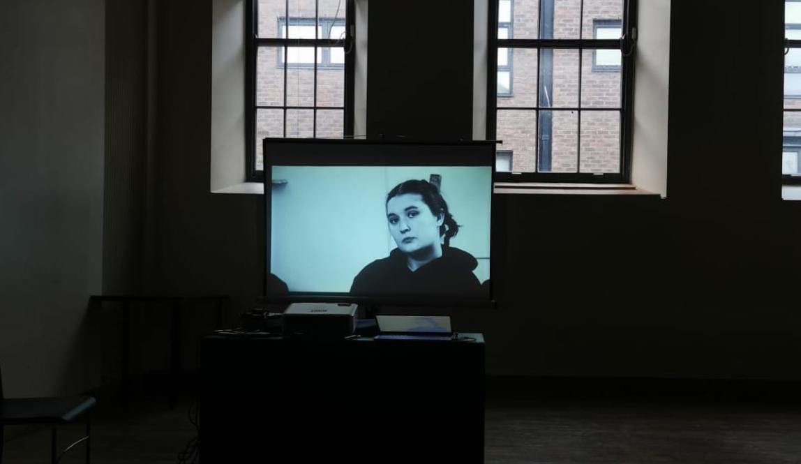 In the center of a dark classroom, there is a television screen with Mariana's face on it. 