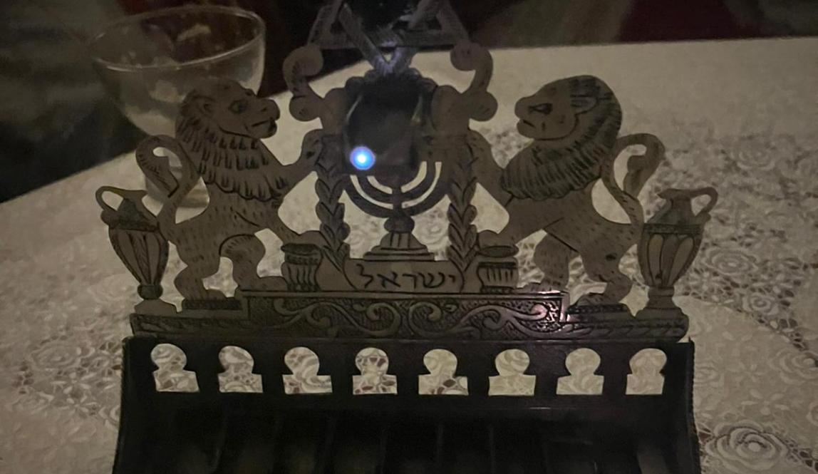 An oil lamp chanukiah with two Barbary lions framing a Star of David. The Shamas and the first light are lit.