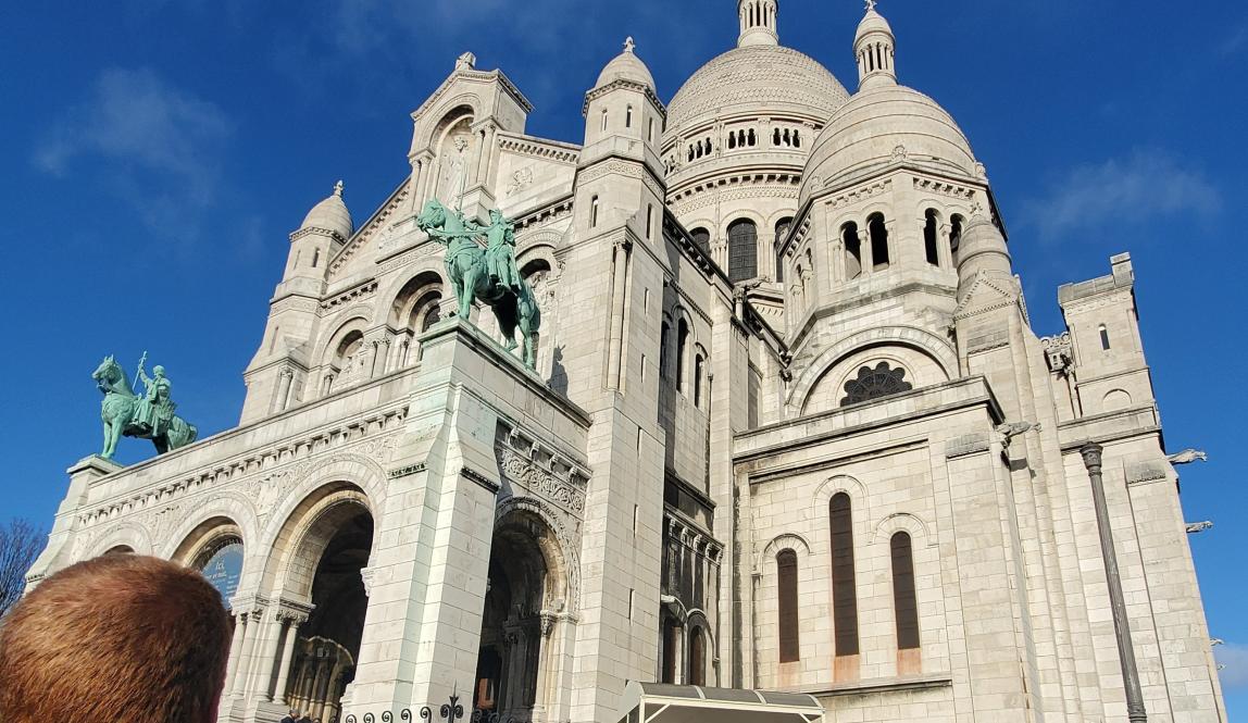The Sacre-Coeur with a blue sky behind it and a ginger head blocking the bottom left corner.
