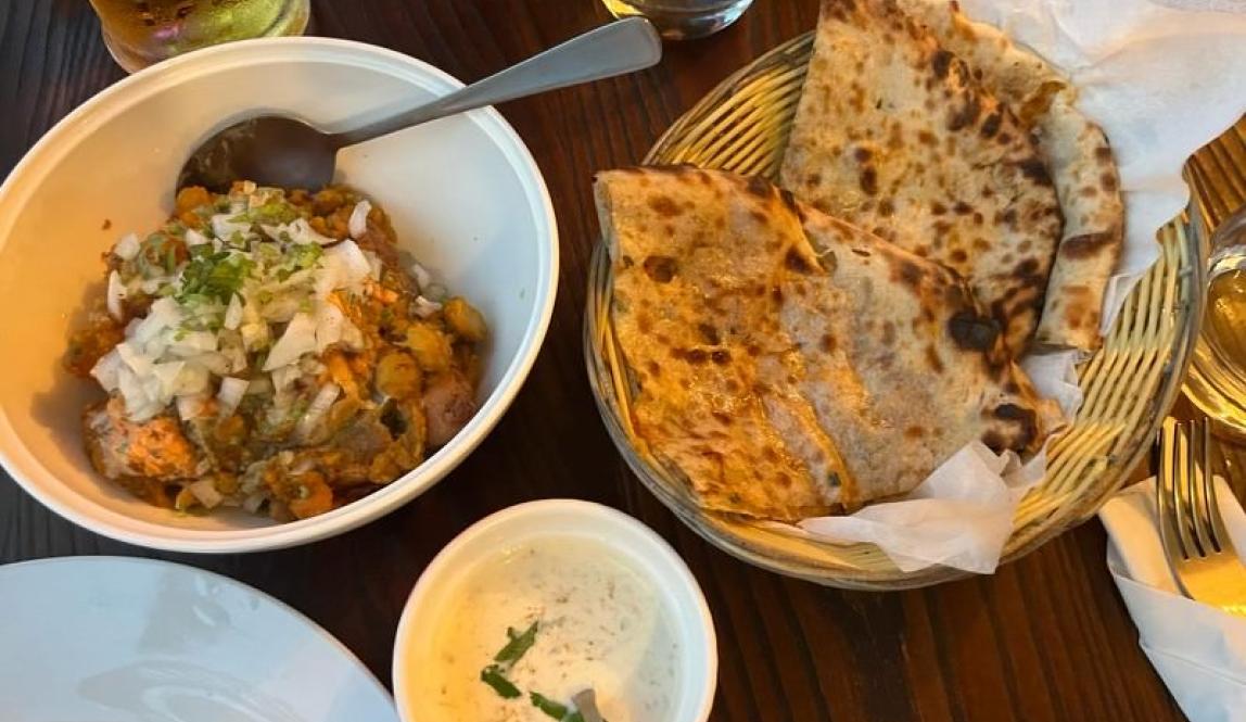 In this photo there is paratha which is a flatbread that is fried in a pan and samosa chaat which is made with curry, chopped up samosa, and chutney.