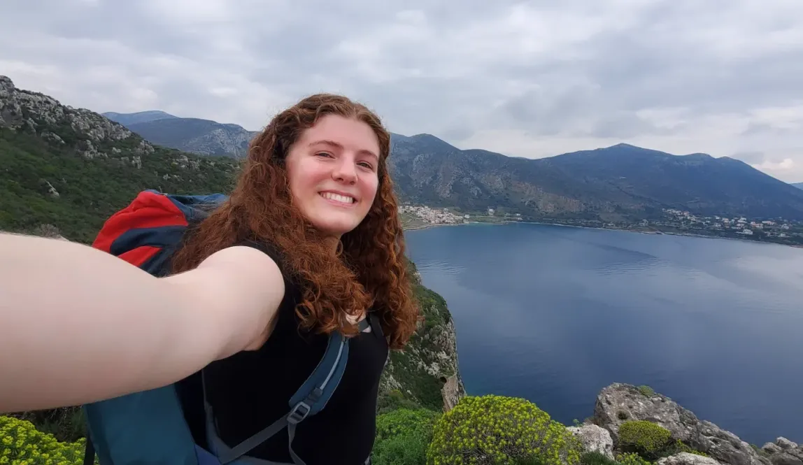 A ginger girl smiling into the camera with a scenic background behind her.