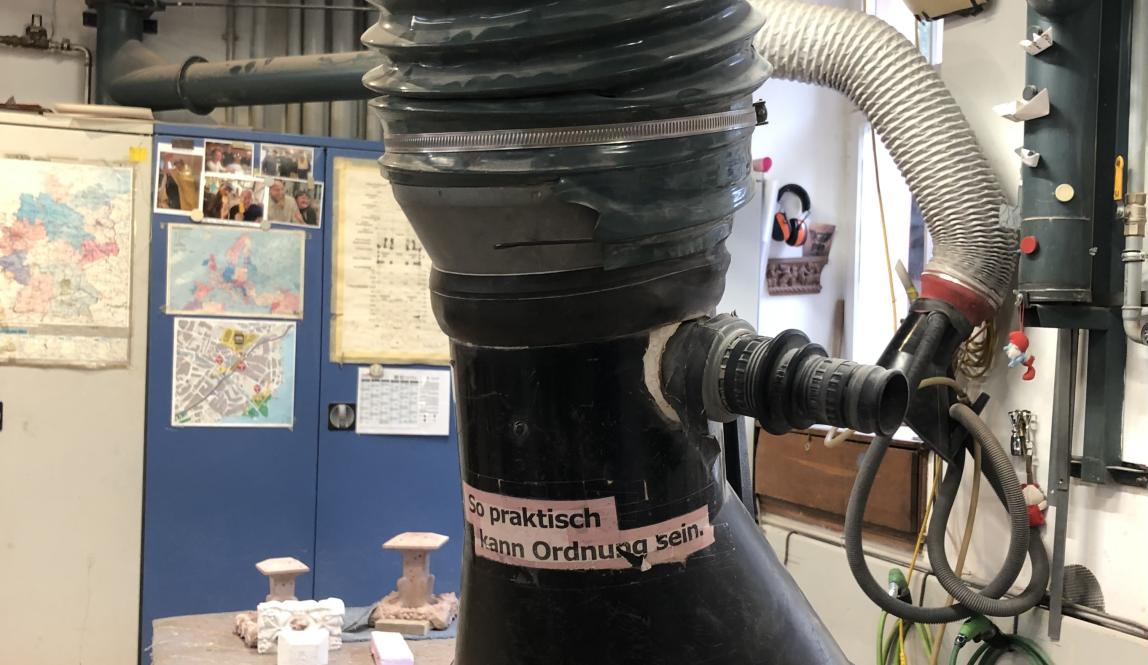 Sticker displaying words: "So praktisch kann Ordnung sein" on black mechanical pipe.  