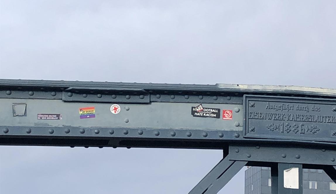 Various political-themed stickers displayed on blue footbridge. Blue sky in background.
