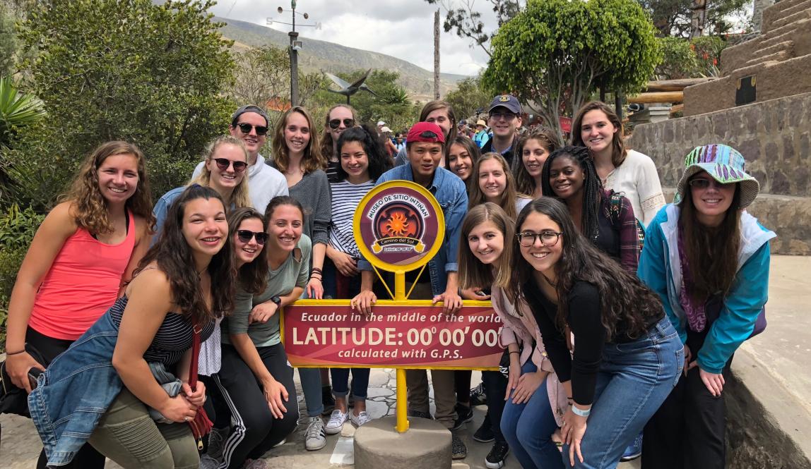 a group of students pose for a photo next to the 0 latitude line at Mitad del Mundo