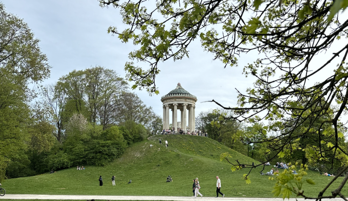 A photo of the english gardens with a big, white, circular building with pillars sitting on top of a tall hill 