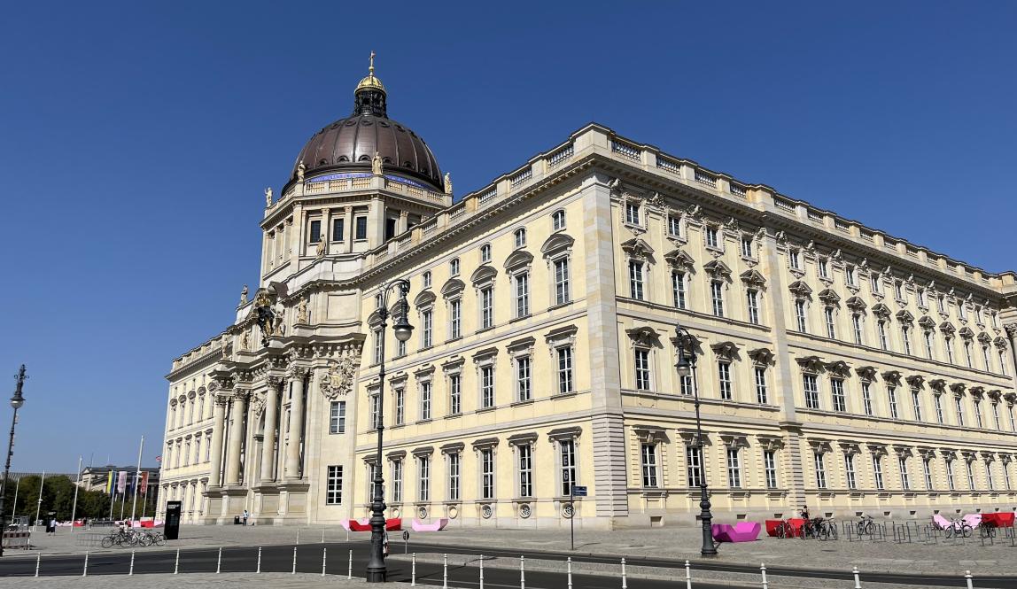 An imposing building is in the forefront, with a clear blue sky behind it. 