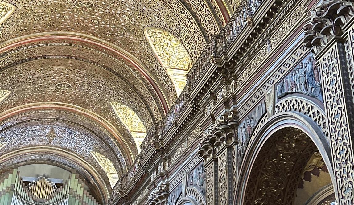 An interior image of an ornate, arched church ceiling. Intricate gold across the ceiling.