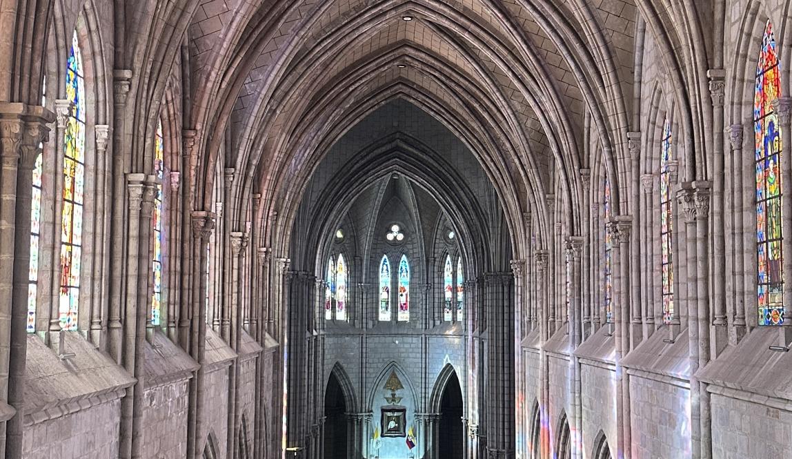 The interior of the Basílica del Voto Nacional. Arched ceiling with large stained glass windows.