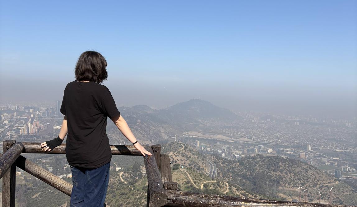 Student looking out at a view of Santiago from a wooden platform at a viewpoint on the Cerro El Carbón trail