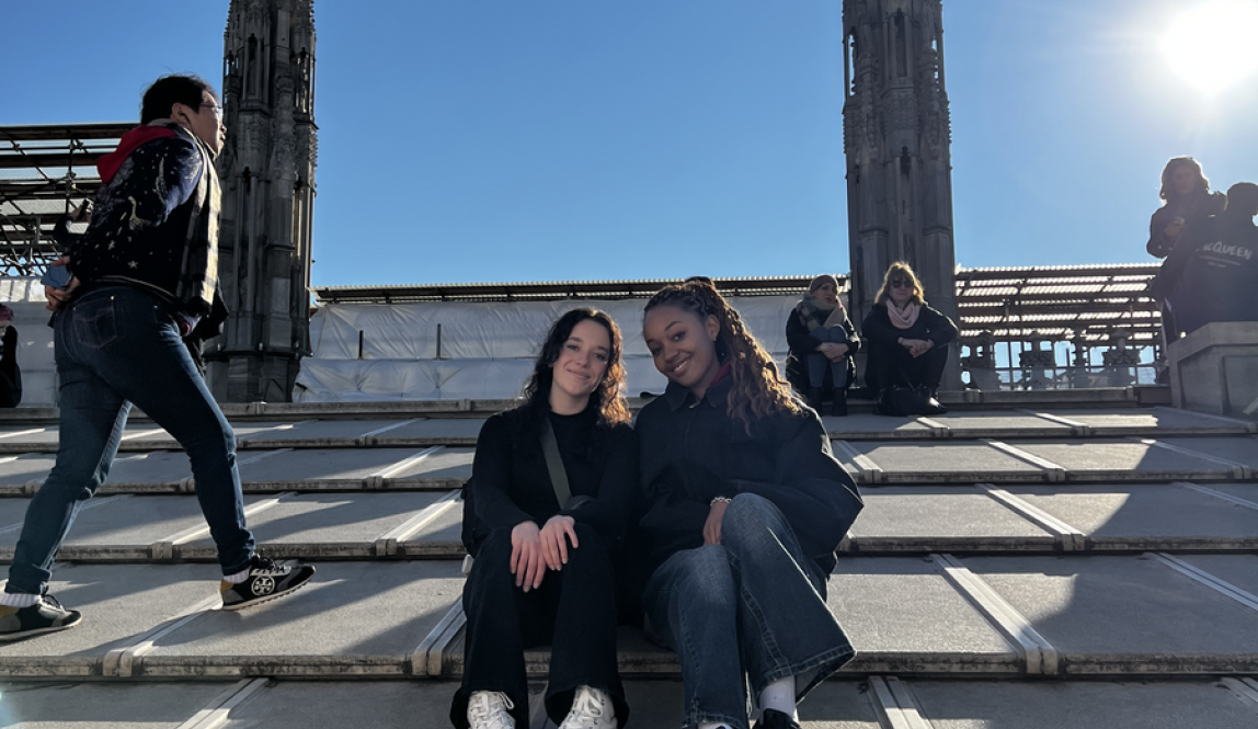Two friends sitting on the roof of the Milan Duomo with other people in the background and sun shining down