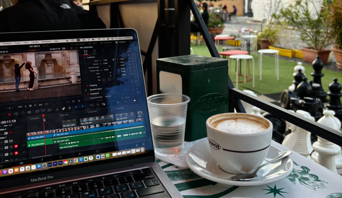 A cup of coffee and a laptop with video editing software at a cafe in front of the Colosseum.