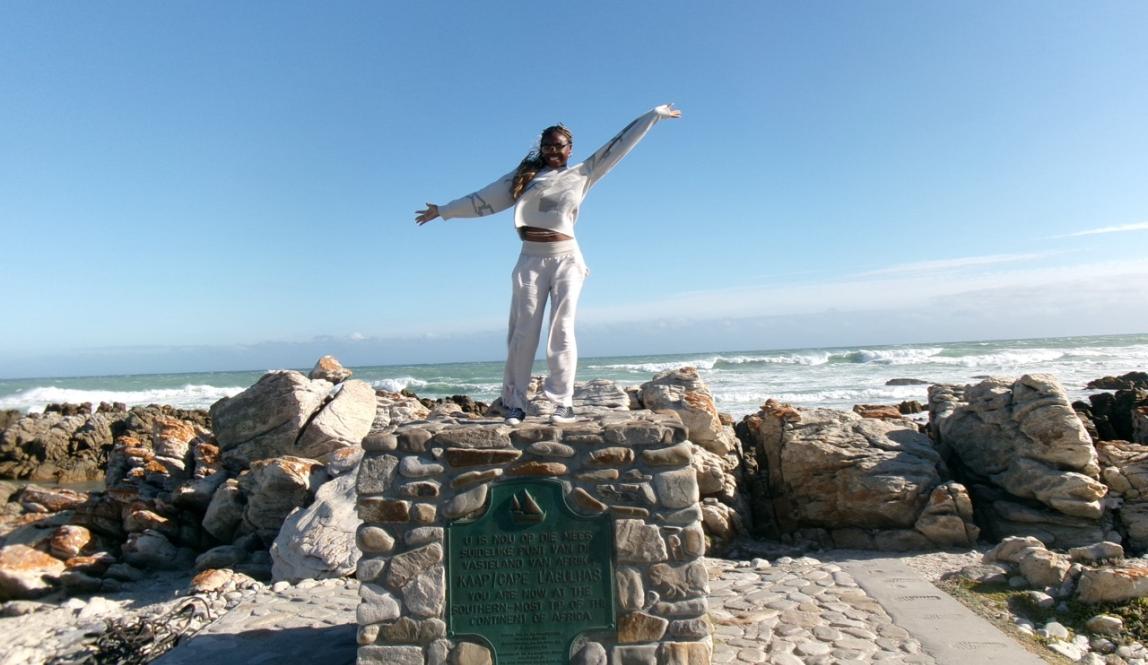 Picture of me on a structured pile of rocks with a plaque reading that where I am is Africa’s southernmost point. East of this is the Indian Ocean, and west is the Atlantic Ocean.