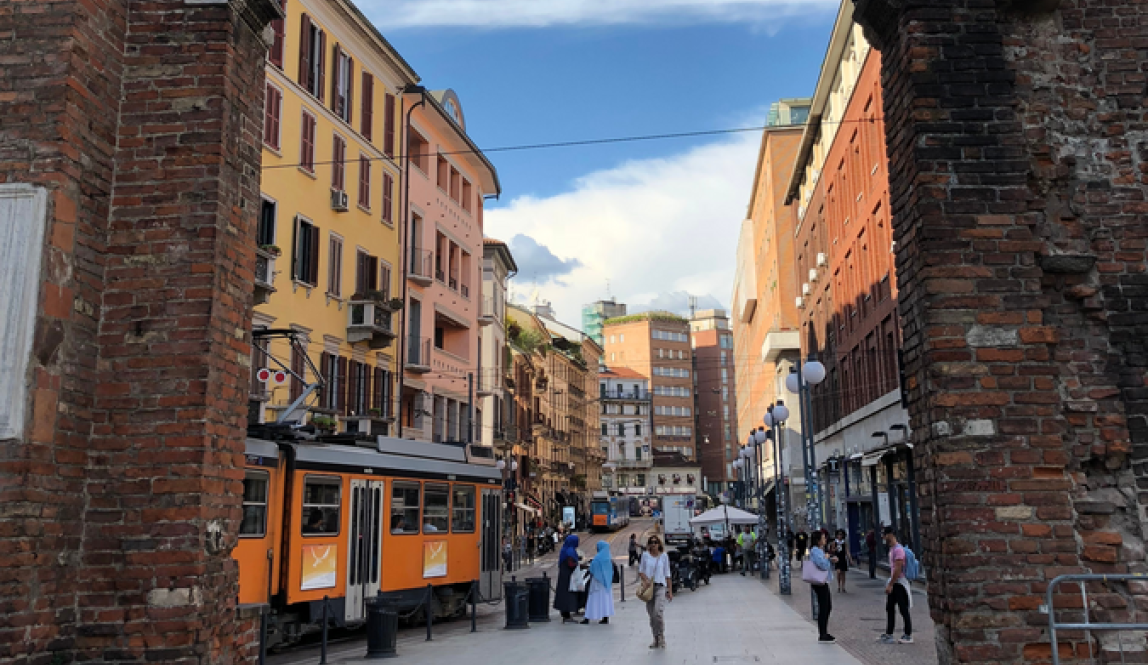 A bustling Milan street as viewed through a historic archway