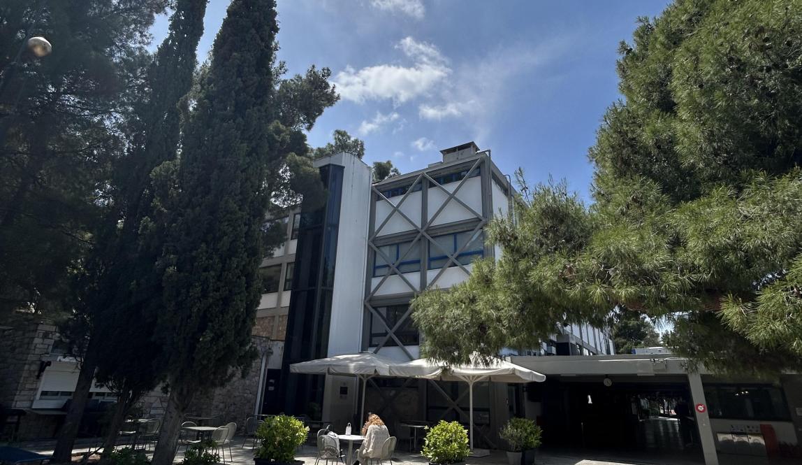 Modern building surrounded by trees under a clear blue sky. This alt text was added with Al; accuracy may vary.