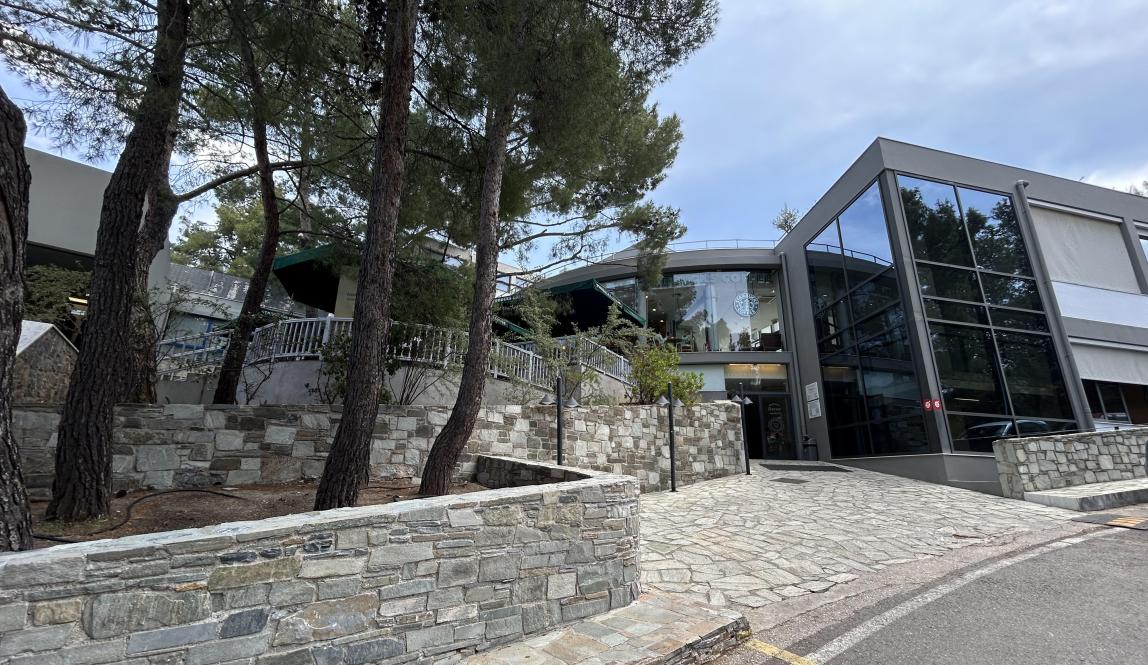 Modern building with stone walls, glass facade, surrounded by trees under a cloudy sky. This alt text was added with Al; accuracy may vary.