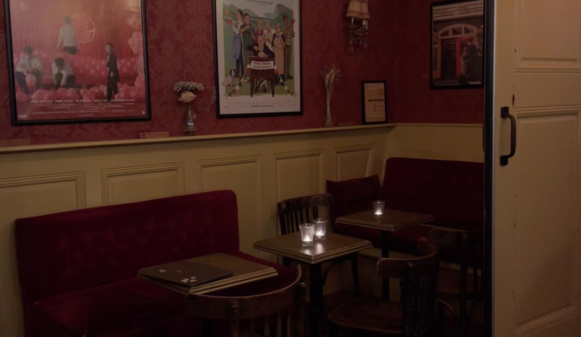 A table crammed into the corner of a low-lit bar. The table has two seats and is paired with movie posted plastered onto the neighboring wall.