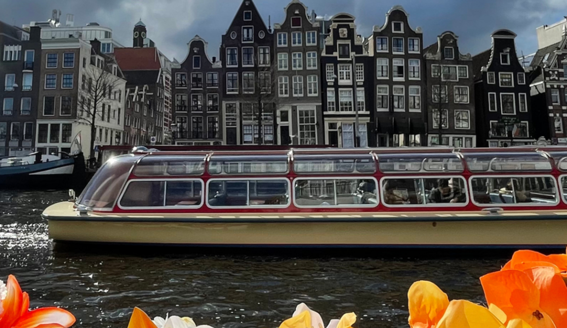 Flowers in front of the water in Amsterdam, along with a boat and buildings in the background
