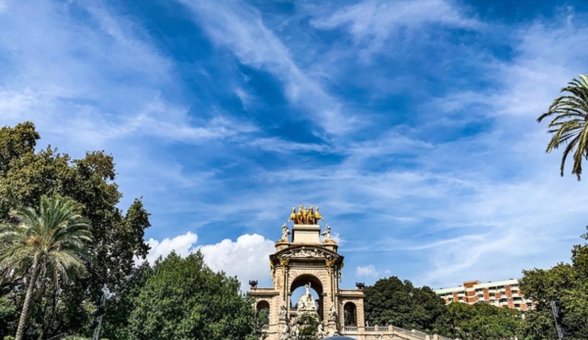 The Arc de Triomf in Barcelona, with a clear blue sky, palm trees, and a reflective sphere in front