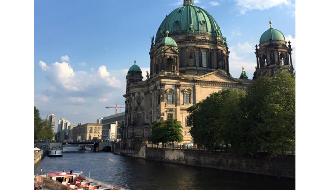 The Berliner Dom with its green dome beside the Spree River, with a boat in the foreground and a blue sky above.