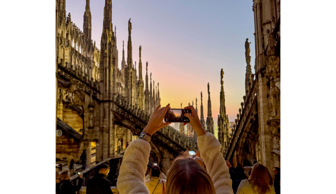 Girl taking a photo at sunset on the rooftop of the Duomo in Milan, surrounded by intricate Gothic spires.