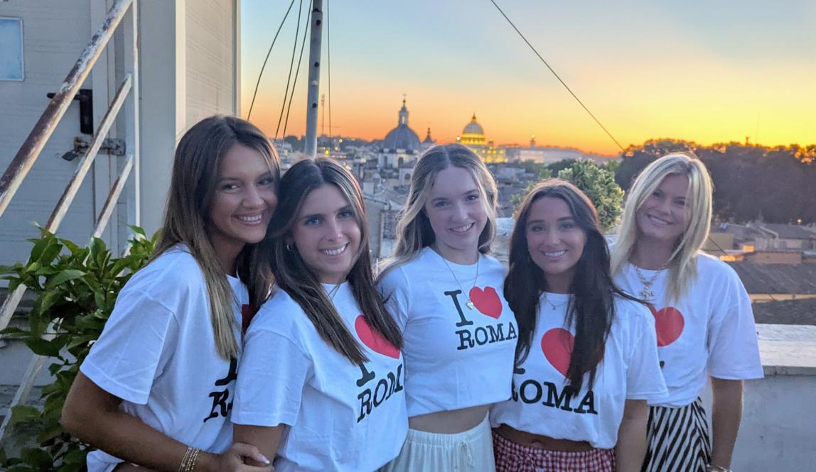 Five students smile in front of a sunset wearing I heart Roma t-shirts.