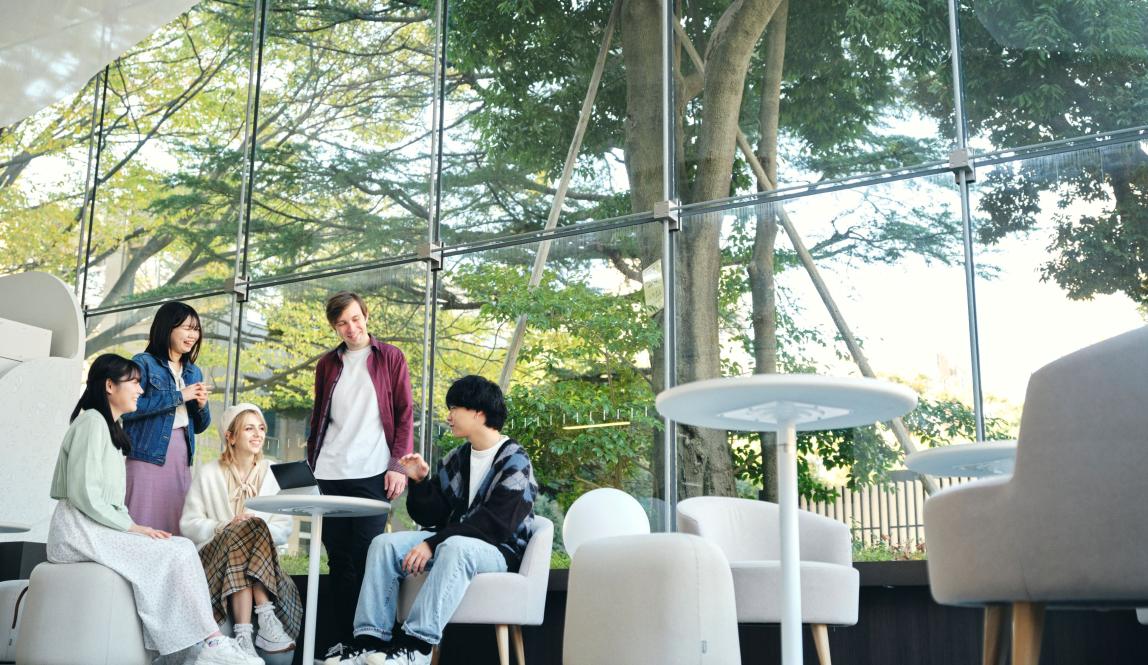 Students sitting and smiling indoors near a window at Musashi University