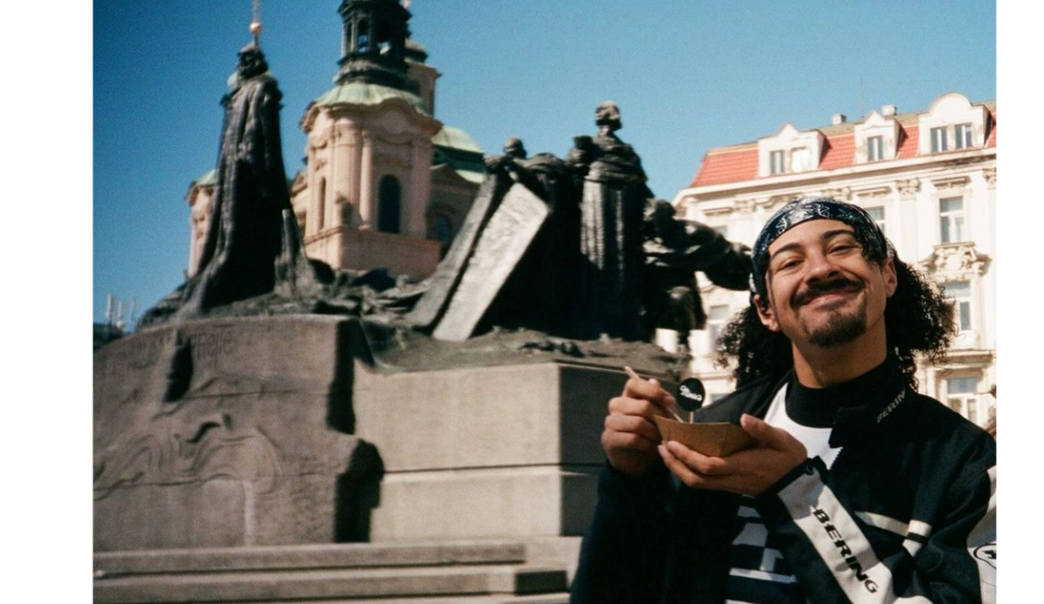 A boy holding a small bowl in front of a historic statue and church towers in berlin on a sunny day.