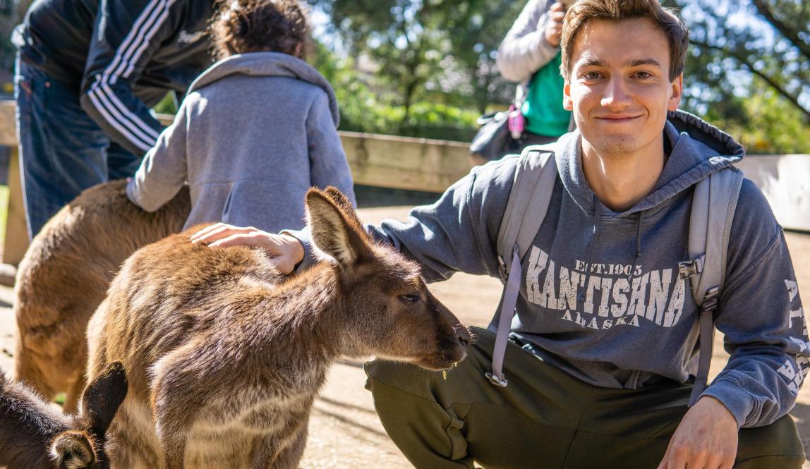 A male student kneeling down with his hand on a kangaroo