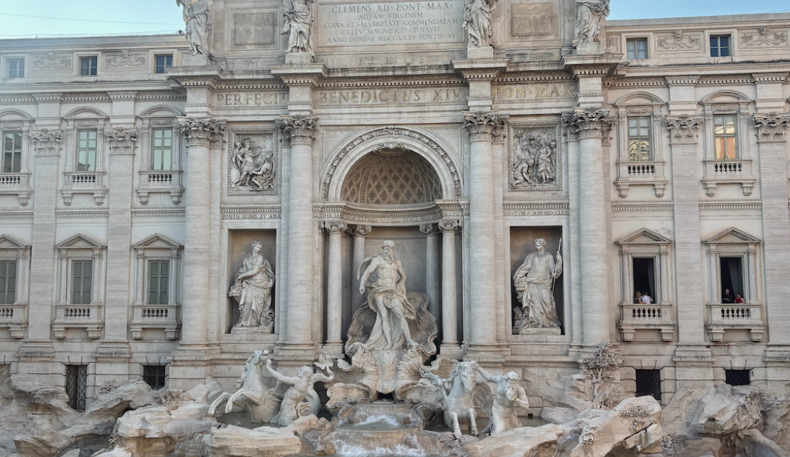 The Trevi Fountain in the evening from a second floor store window with crowds of toursits gathered around the edge of the fountain.