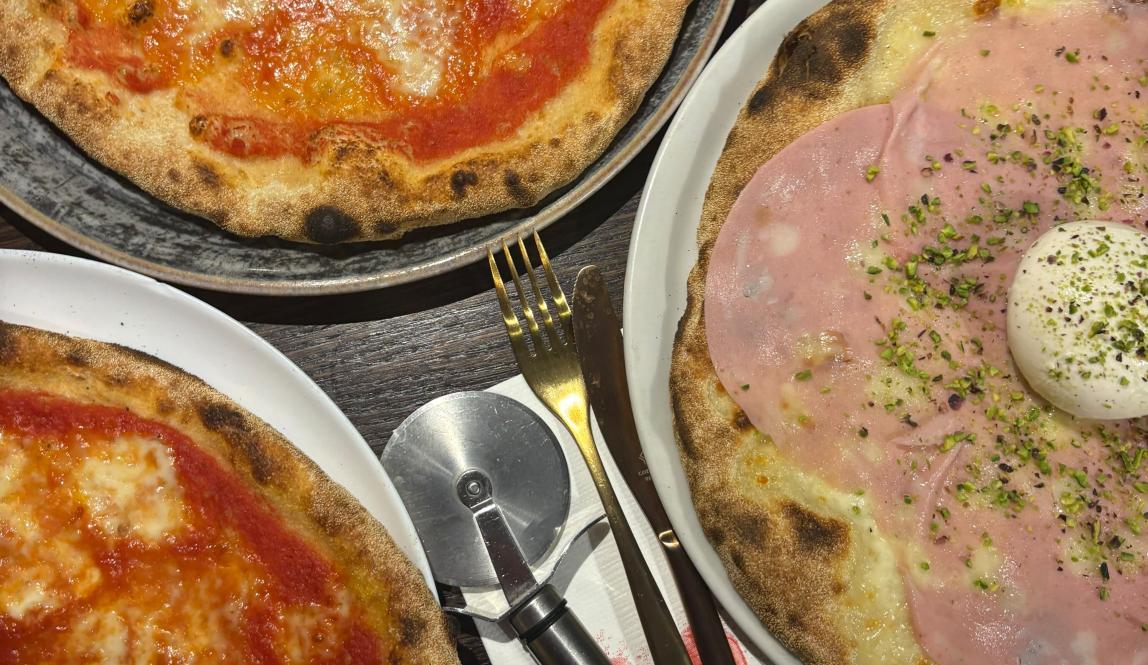 Three pizzas on plates at a dinner table.