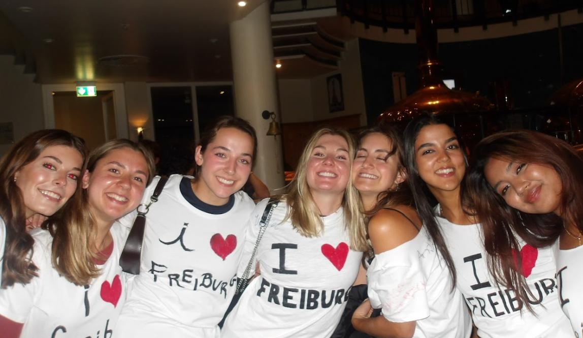 Seven girls smile and pose in homemade "I heart Freiburg" shirts.