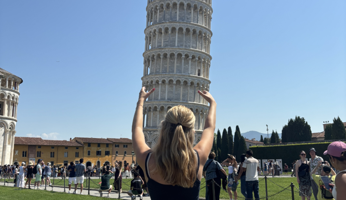 The Leaning Tower of Pisa with a girl posing in front as if she is holding up the leaning tower.