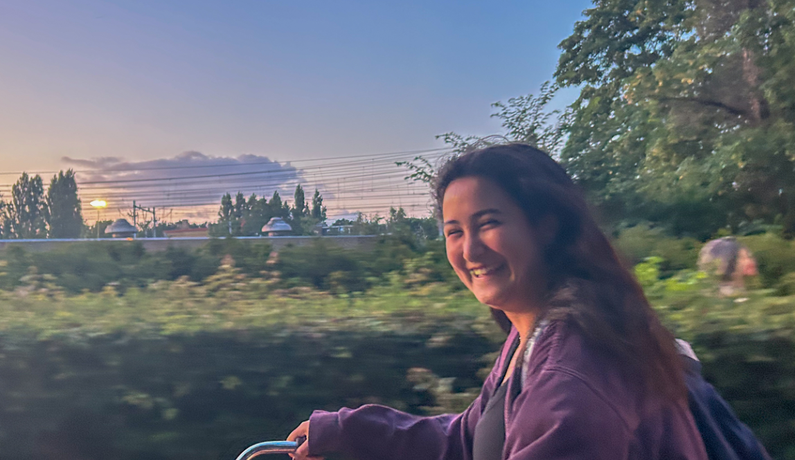 A student riding their bike and smiling with the sunsetting in the background.