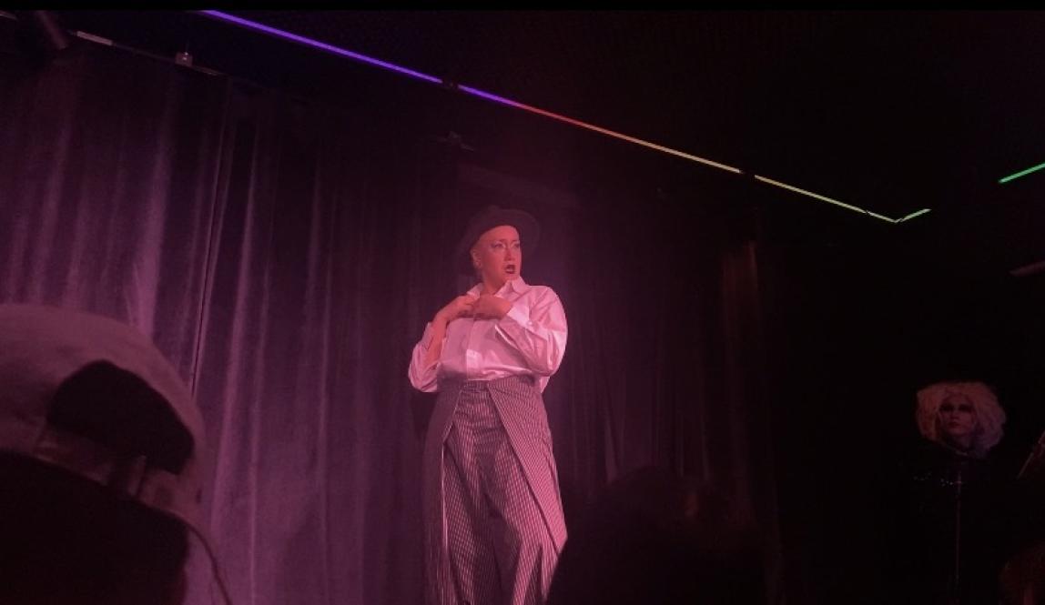 A drag performer in a black and white suit under pink lighting.