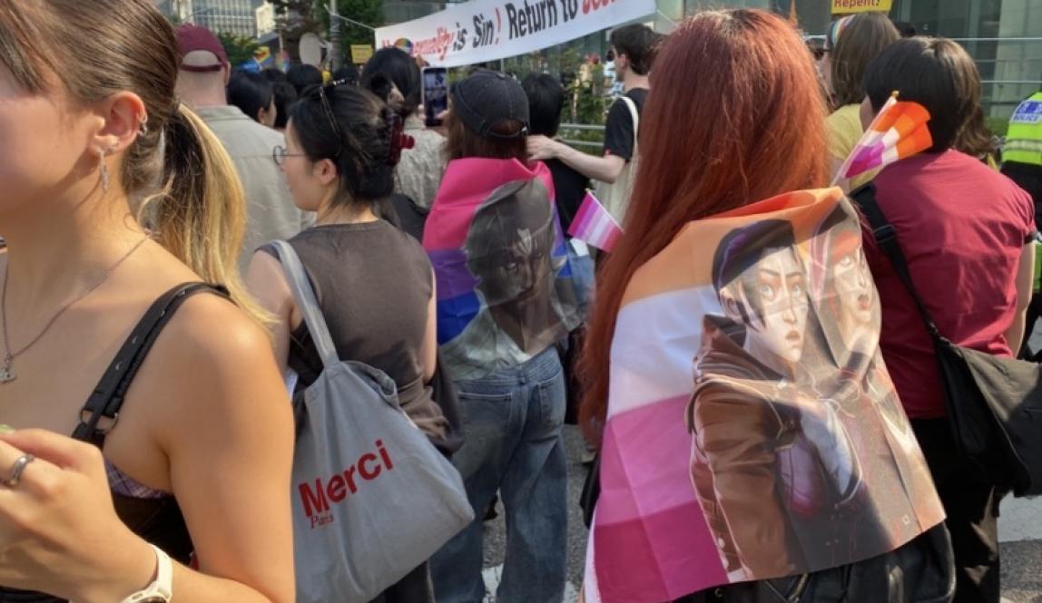 Festival attendees carrying lesbian pride flags with banners that read "Homosexuality is sin! Return to Jesus!" and "Homo sex is sin! Repent!" in the background.