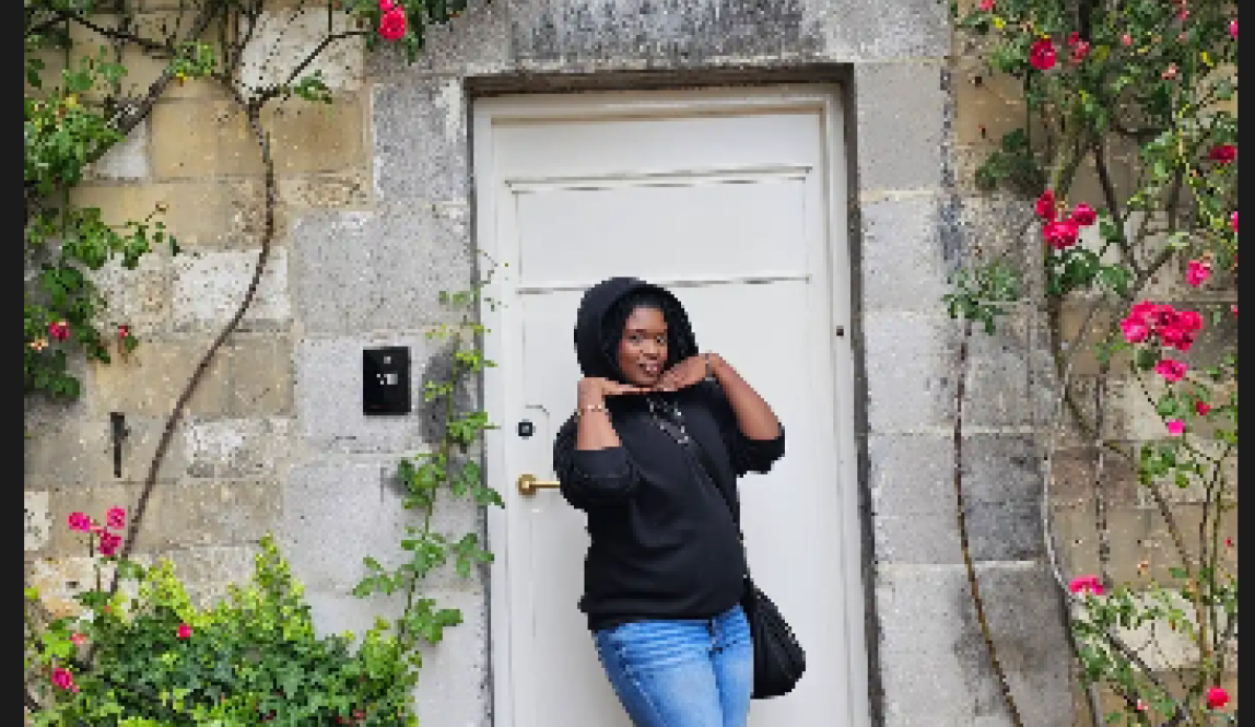 The author of this blog is posing in front of a white door that is the backdrop of a pink floral arch in Maastricht 