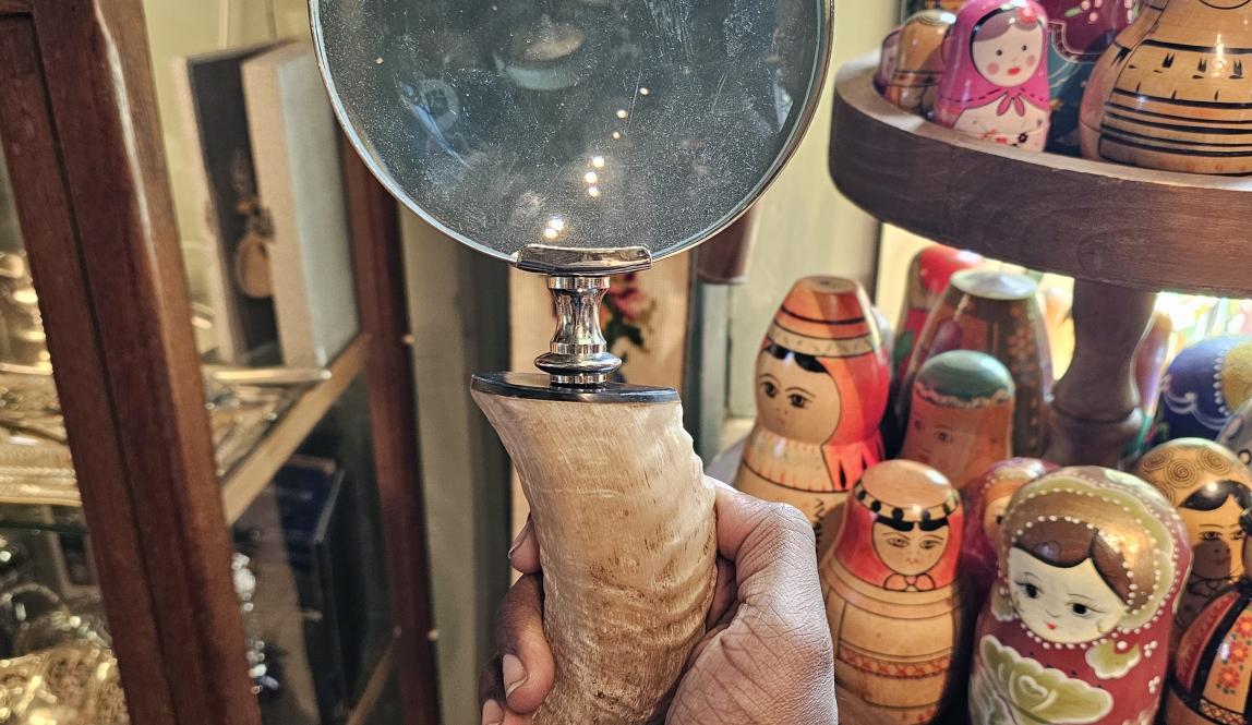 The author is holding a magnifying glass by its handle in front of him displaying the craftmanship of an animal tusk used as its handle.